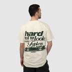 A man viewed from behind wearing a cream-colored t-shirt with a dark green graphic print on the back. The graphic features the text 'hard not to look WHEN Topless' above a silhouette of a classic car, with 'another.