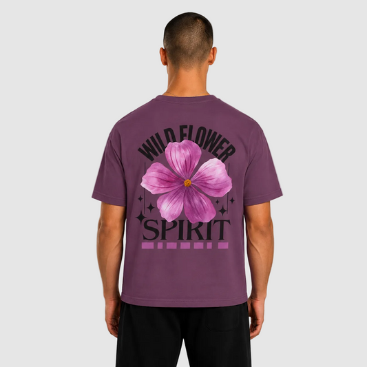 A man viewed from the back wearing a purple short-sleeve t-shirt with a large graphic on the back. The graphic features a pink hibiscus flower in the center, with the words 'WILD FLOWER SPIRIT' in black arched above and below the flower.